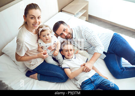 La famiglia felice giocando giacente sul letto in camera da letto. Foto Stock