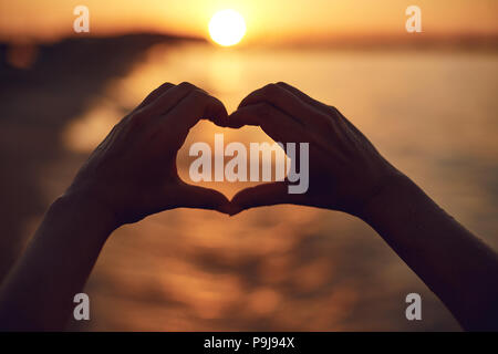 Le mani a forma di cuore sul tramonto sul mare. Foto Stock