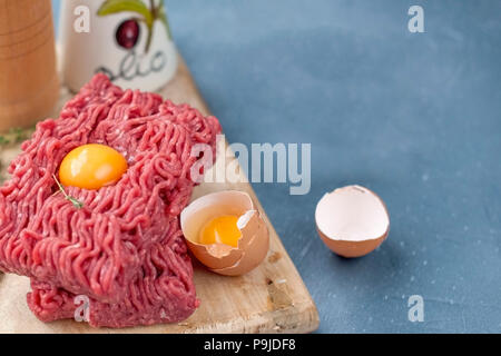 Carni fresche bovine carni macinate, su una tavola di legno.visto uova. Su una pietra grigia sullo sfondo. Spazio libero per la scrittura di testo Foto Stock
