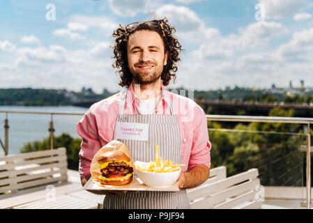 Il fast food lavoratore portando hamburger con patatine fritte per i suoi clienti Foto Stock