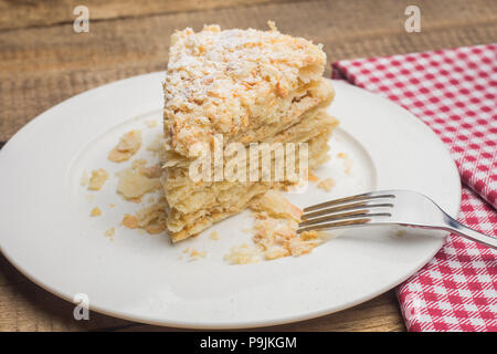 Torta Napoleone su una piastra bianca, su uno sfondo di legno e un rosso Foto Stock