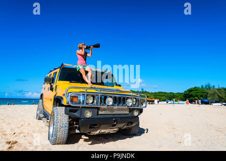 Donna con fotocamera si siede sulla jeep sulla spiaggia Foto Stock