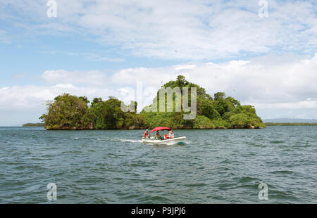 Cayo o isola di roccia, fregate volteggiare sopra, davanti un motoscafo, Parco Nazionale Los Haitises, Samaná Provincia Foto Stock