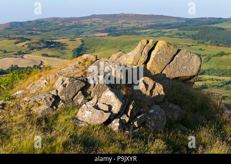 Una formazione rocciosa sulla collina Corndon, Powys, con la Stiperstones, Shropshire, all'orizzonte. Foto Stock