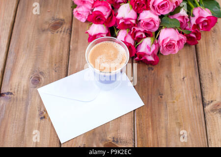 Un profumo di rosa fresca rose e un bicchiere di caffè espresso. Sfondo di legno. Spazio libero per il testo o per cartoline. Busta bianca per iscritto. Foto Stock