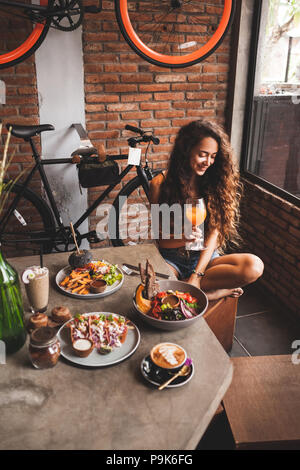 Donna godendo organico fresco cibo vegetariano e vetro del Kombucha in stile hipster cafe con design di bicicletta Foto Stock