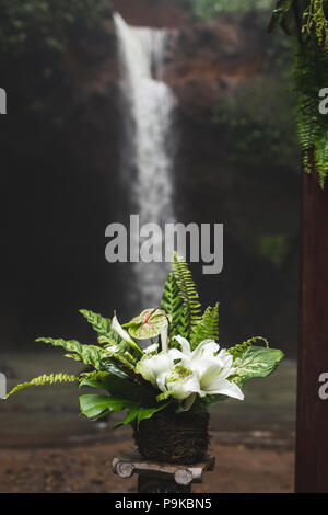 Tropical cerimonia di nozze con vista cascata. Arco bianco decorato con giungla verde lascia monstera e fern Foto Stock