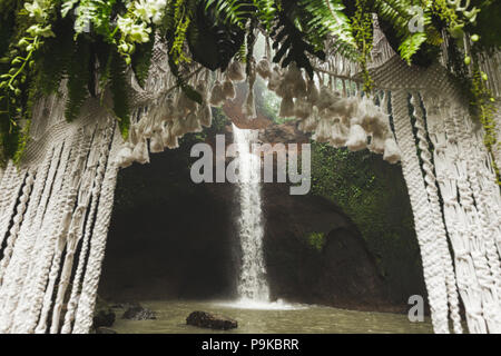 Tropical cerimonia di nozze con vista cascata. Arco bianco decorato con giungla verde lascia monstera e fern Foto Stock