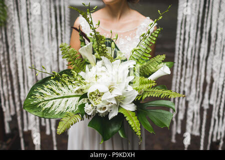 Sposa tenendo in mano un enorme bouquet di verde con foglie tropicali e fiori Foto Stock