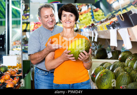 Adulto felice positivo maschio e femmina sono la scelta di verde di meloni in negozio. Foto Stock