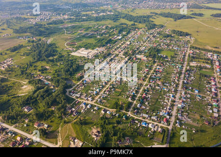 Elicottero drone shot. Vista da sopra su un piccolo villaggio, motore road, foresta verde e un grande campo in una calda e soleggiata giornata estiva Foto Stock