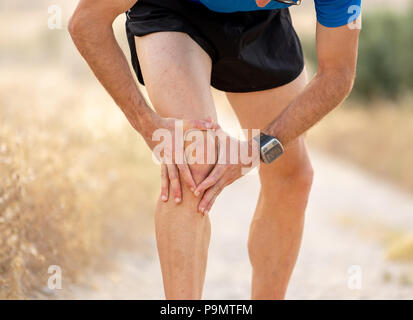 Close up uomo con forte gambe atletiche holding ginocchio con le sue mani nel dolore dopo aver subito un infortunio muscolare durante l'esecuzione di un processo di formazione di allenamento in asfalto Foto Stock