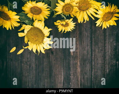 Un bouquet di fioritura giallo dei girasoli su un di legno marrone, sfondo vintage tonificante, spazio copia Foto Stock