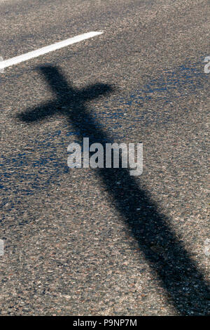 L'ombra della croce cristiana sull'asfalto, formata dall'illuminazione del sole da una vecchia Croce di legno vicino al villaggio, close-up Foto Stock