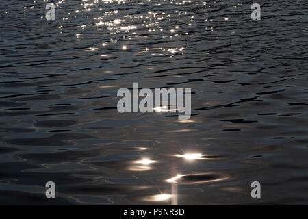 Bianco bagliore del sole sull'acqua scura del lago, close-up in autunno è al di fuori della messa a fuoco Foto Stock