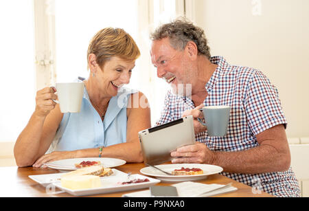 Felice attraente senior coppia matura utilizzando computer tablet navigare su internet mentre si consuma la colazione e di bere il caffè a casa. Età Communicat Foto Stock
