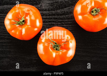 3 pomodoro rosso isolato nero su uno sfondo di legno vista superiore Foto Stock