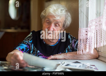 Donna anziana guardando le foto seduta a tavola. Foto Stock