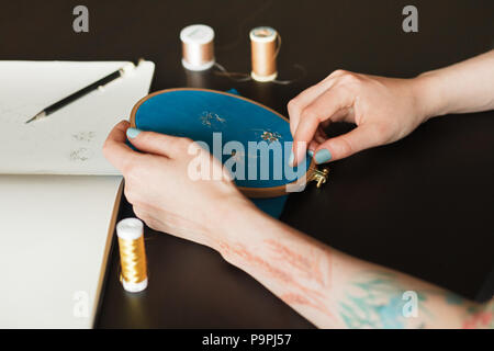 Workplace ricamatori: contorno in un notepad, ricami hoop, forbici e thread. Le mani del master Foto Stock