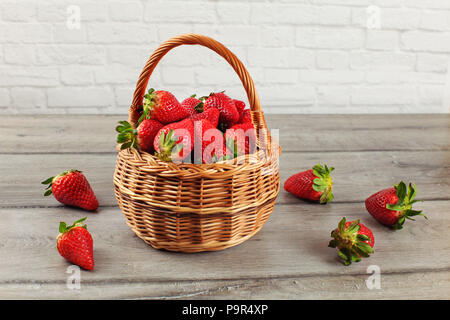 Cesto di Fragole, alcuni di loro versato sul legno grigio desk. Foto Stock