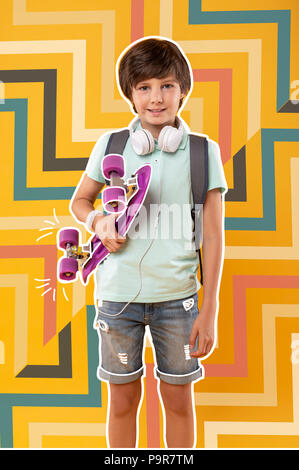 Sorridente ragazzo di indossare un abbigliamento informale e godendo di cavalcare uno skateboard Foto Stock