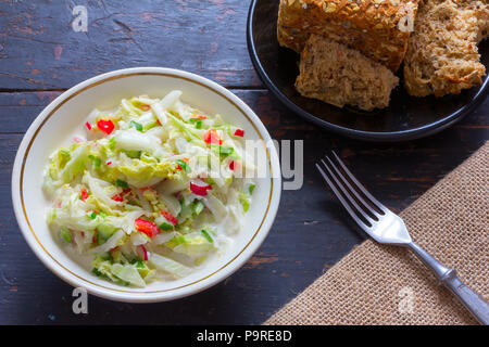 Insalata di verdure fatta di cavoli freschi, rafano, cetriolo, peperone e panna acida in una piastra bianca, cornbread e tappo nero sul vecchio PC desktop. Top vie Foto Stock