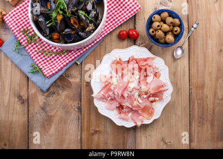 Muesli in un bianco di ceramica ciotola, su un tovagliolo rosso. Olive, pane. La carne su un piatto. Su uno sfondo di legno. Spazio libero per il testo o per la pubblicità Foto Stock