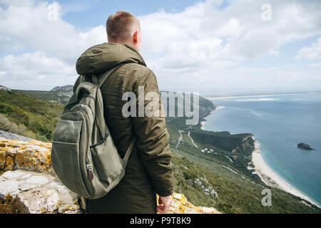 Un turista o viaggiatore con lo zaino è in piedi sulla cima di una collina e ammirare la splendida vista sull'oceano o sul mare. Passeggiate o escursioni. Foto Stock