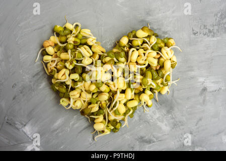 Forma di cuore fatta da fagioli con i germogli sul cemento grigio sfondo Foto Stock