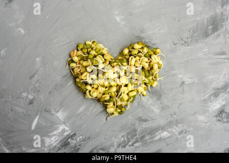 Forma di cuore fatta da fagioli con i germogli sul cemento grigio sfondo Foto Stock