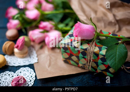 Un bouquet di rose rosa, una scatola con un regalo. Pasta dolce amaretti di diversi colori, il giorno di San Valentino Foto Stock