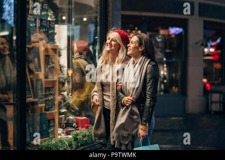 Vista laterale di due metà donne adulte alla ricerca di un negozio finestra mentre facendo un po' di shopping natalizio. Foto Stock