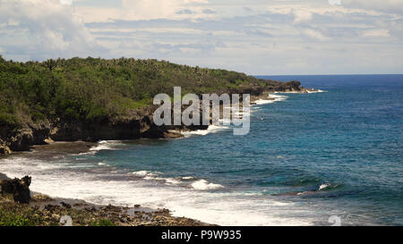 Spiaggia rocciosa con palme, acqua blu su un isola tropicale. Mare costa rocciosa, di onde che si infrangono al litorale roccioso. Punto di vista lungo la spiaggia sassosa con rocce.sassoso mare spiaggia scena. Filippine. Concetto di viaggio. Foto Stock
