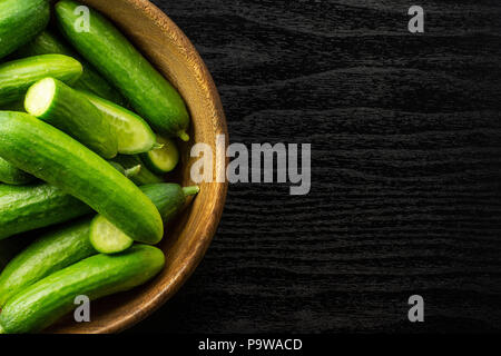 Mini fresco cetrioli in una ciotola di legno flatlay nero su uno sfondo di legno Foto Stock