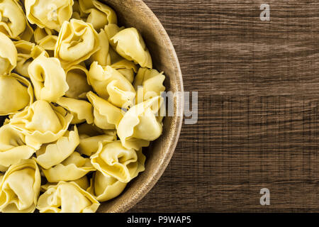 Materie tortellini in una ciotola di legno flatlay marrone su uno sfondo di legno tradizionale italiano gnocco Foto Stock