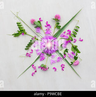 Un bouquet di vari fiori viola con foglie verdi su sfondo grigio. Piatto, laici vista superiore Foto Stock