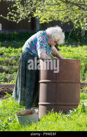 Vecchia donna nel giardino in una botte di ferro con acqua Foto Stock