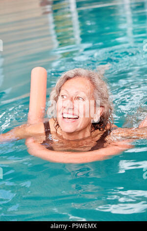 Vitale donna senior è di imparare a nuotare con noodle al nuoto in piscina Foto Stock