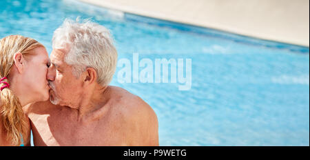 Senior amorosa giovane kissing nella piscina dell'hotel in vacanza Foto Stock