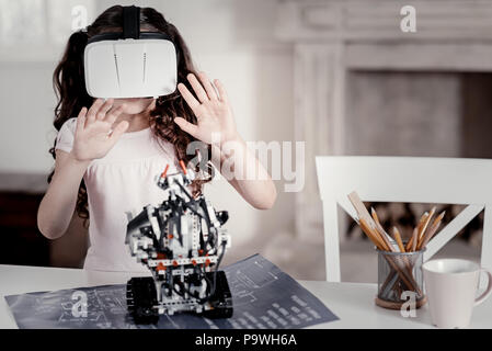 Non conosce limiti. Poco carino ragazza indossando occhiali VR vedendo il suo giocattolo in piedi sulla tavola come nella vita reale Foto Stock