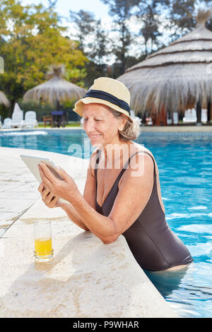 Senior donna sul bordo della piscina in hotel Piscina con computer tablet in vacanza Foto Stock