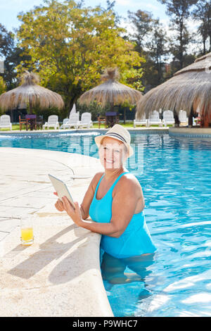 Senior donna sulla vacanza termale in piscina a bordo piscina con computer tablet Foto Stock