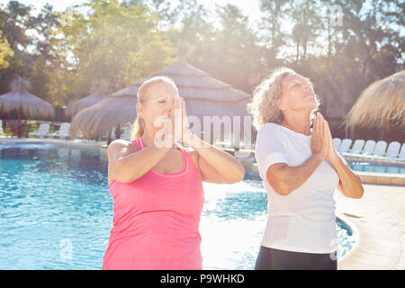 Due donne facendo yoga meditazione insieme presso la piscina durante una vacanza termale Foto Stock