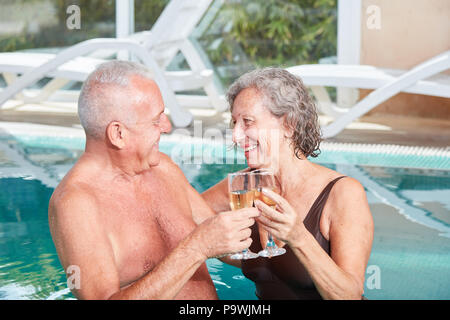 Coppia senior celebrando con un bicchiere di vino frizzante in piscina presso la spa hotel Foto Stock