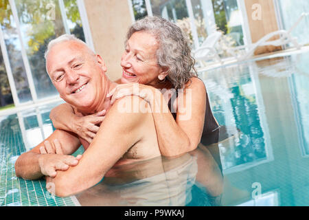 In amore coppia senior abbraccia ogni altro sul bordo della piscina durante una vacanza di benessere Foto Stock