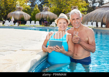 Sorridente coppia Senior utilizzando Tablet In Piscina al Wellness Hotel Foto Stock