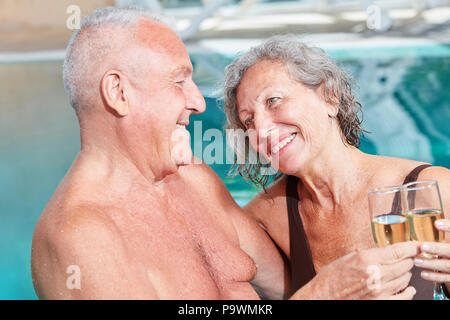 Coppia senior celebra con vino frizzante in piscina durante una vacanza di benessere Foto Stock