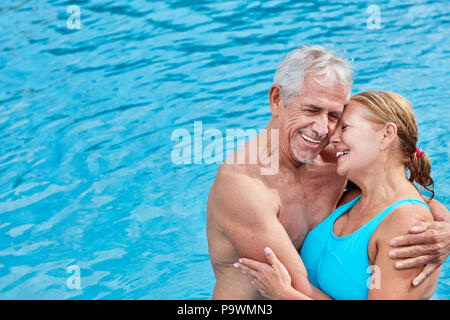 Felice coppia senior in vacanza presso la piscina che abbraccia ogni altra affettuosamente Foto Stock