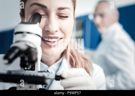 Ritratto di un positivo donna scienziato cercando nel microscopio Foto Stock