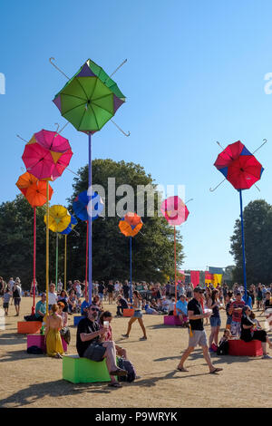 Persone sedersi, passeggiare e godersi l'atmosfera in mezzo a un gruppo di stand con vivacemente colorato ombrelloni attaccati ai poli. Latitude Festival. Foto Stock